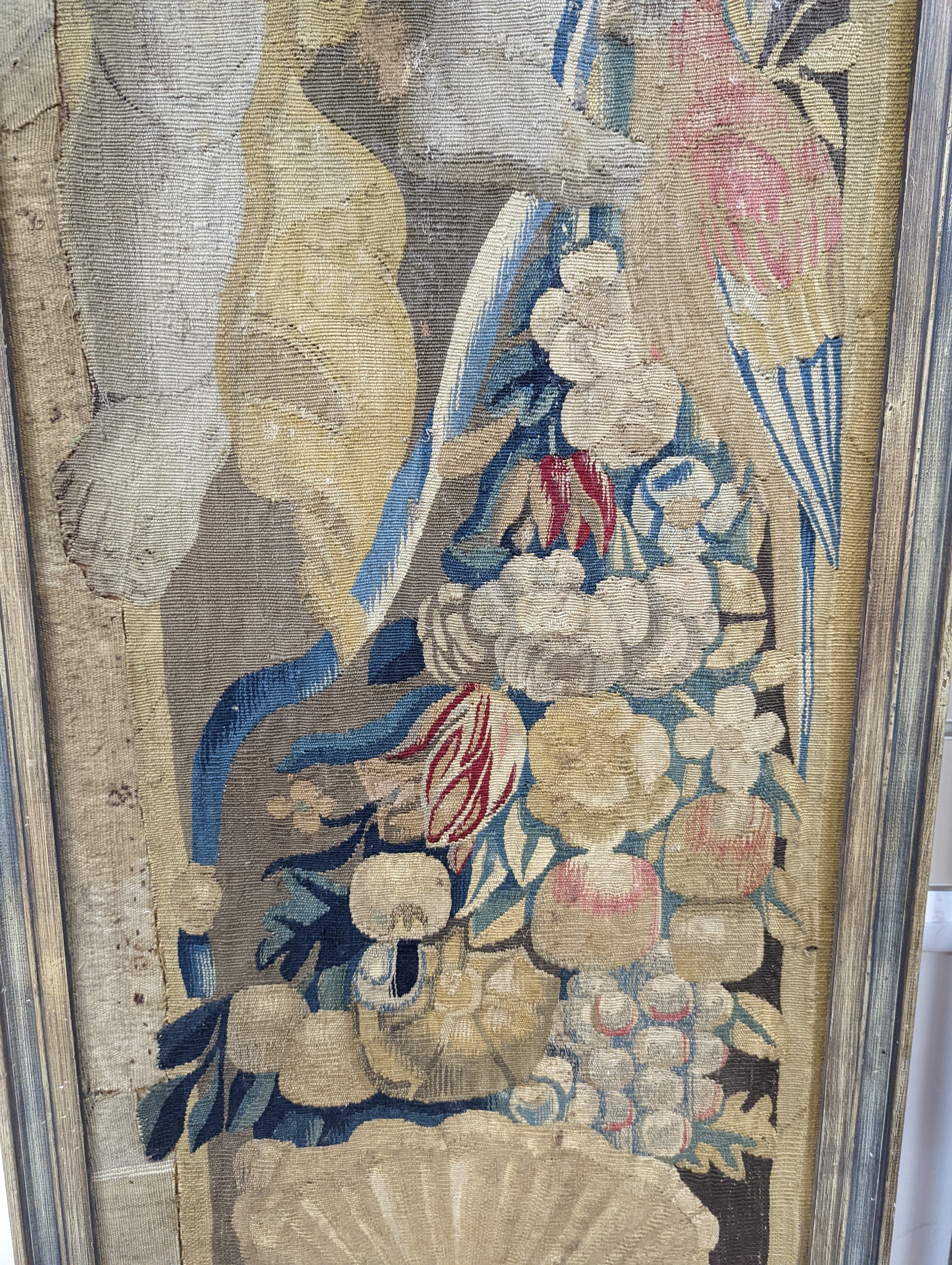 A pair of 17th century Mortlake tapestry panels of cherubs, circa 1660, with flowers, fruit and parrots, standing above scallop shells, later framed, 152 x 41cm, overall 161 x 50cm